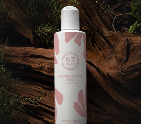 Barrier Boost tonerflaska med rosa mönster står på trä omgiven av grönska, hudvård K-beauty.